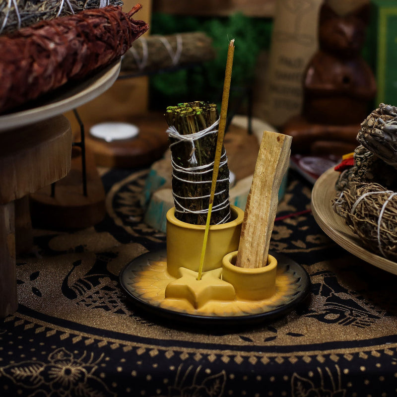 Yellow ceramic holder with sage and wooden stick on a patterned surface