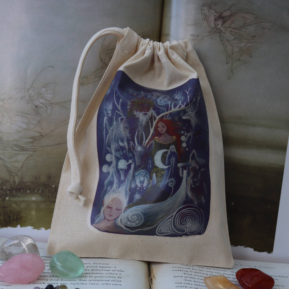 A beige fabric drawstring pouch with a colorful fantasy mermaid illustration, displayed on top of open books with crystals and a beaded necklace around it.