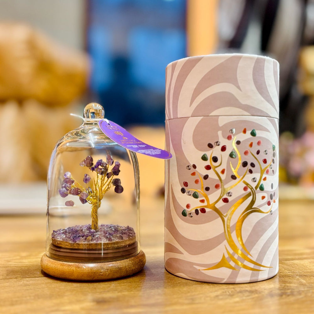 Decorative item with a glass dome containing a small tree and a cylindrical container with a tree design on a wooden surface.
