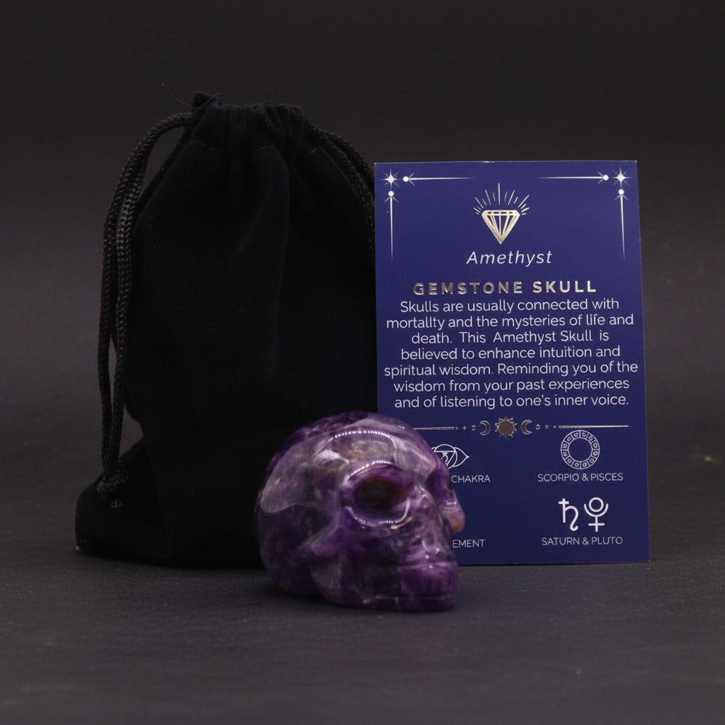 Amethyst gemstone skull with information card and black drawstring bag on a white background. Eleanora Moon