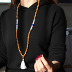 Person wearing a black sweater with a long beaded necklace featuring wooden beads and a white tassel.