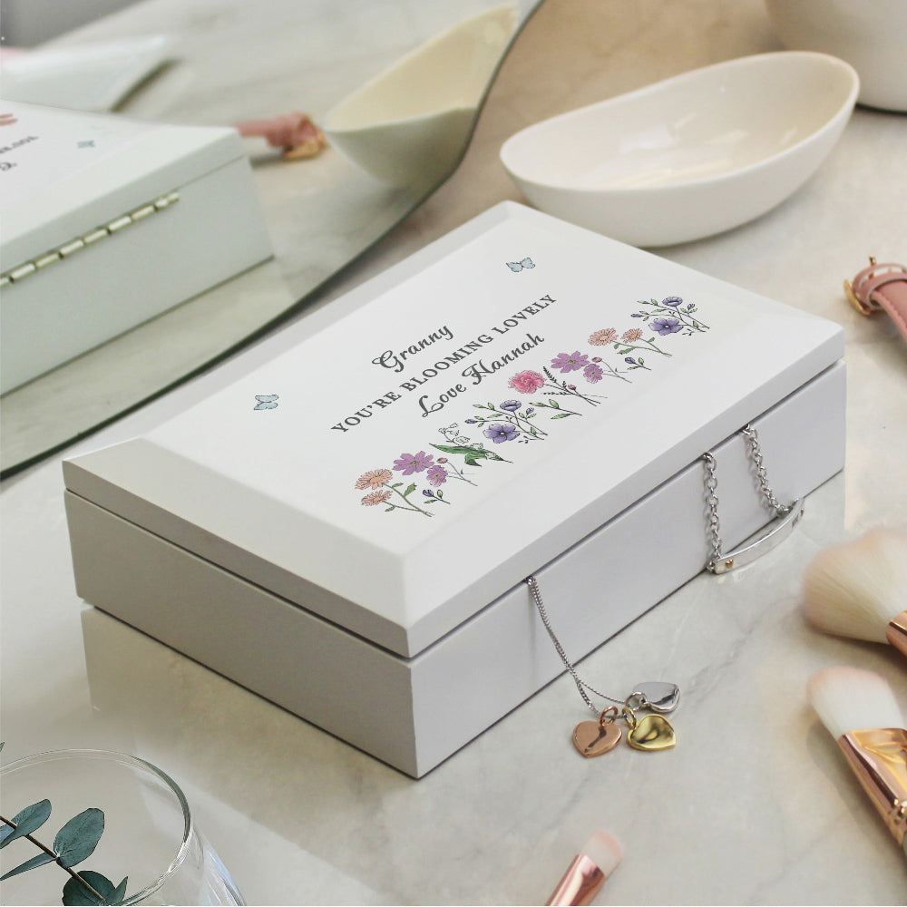 White jewelry box with floral design and engraved text on a light surface.