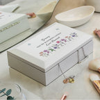 White jewelry box with floral design and engraved text on a light surface.