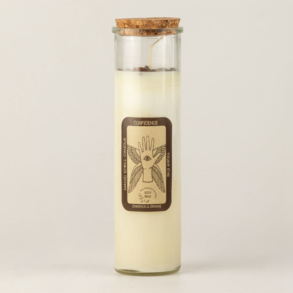 A tall glass jar candle with a cork stopper, filled with creamy off-white wax. The front features a brown label with a hand illustration and the text 'CONFIDENCE' and 'Cinnamon & orange'.