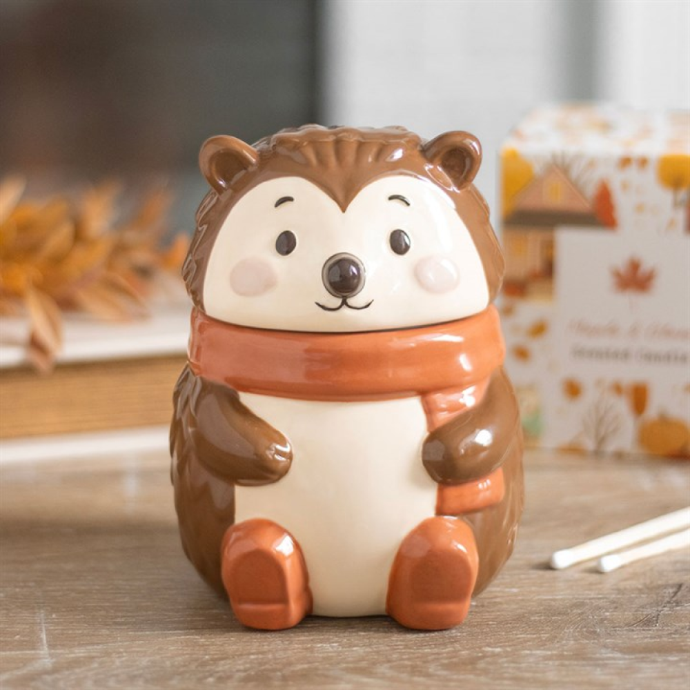 Ceramic hedgehog-shaped oil burner with a scarf on a wooden surface.