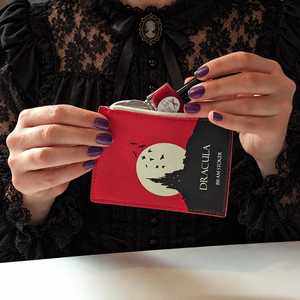 Person holding a red wallet with 'Dracula' design, wearing a black lace top.