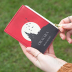 Red book-shaped pouch with 'Dracula' design held by a person against a blurred green background