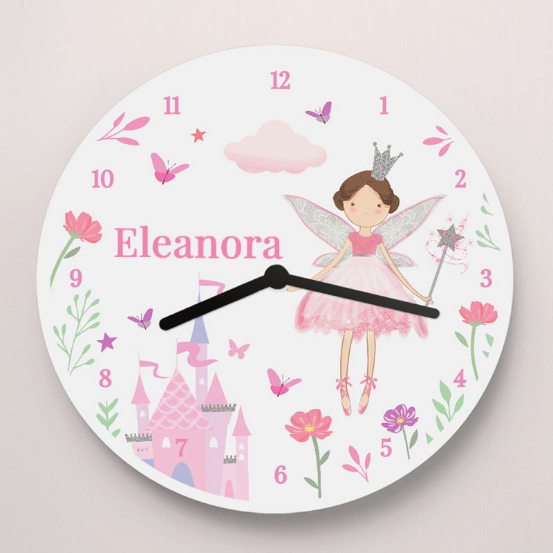 A round children's wall clock with a white face, featuring a pink fairy illustration, a pink castle, butterflies, flowers, and the name 'Eleanora' printed in pink near the center. The clock has black hands and is shown against a light beige background.