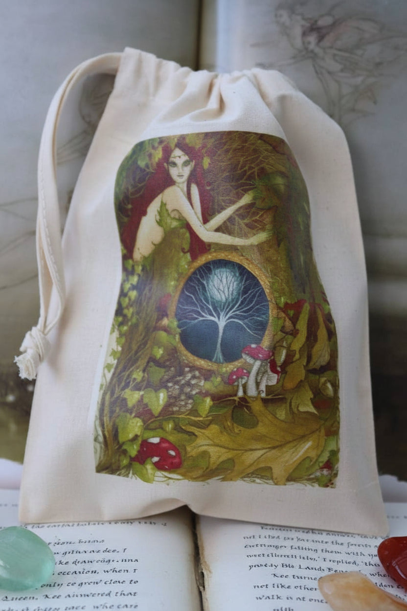 An off-white canvas drawstring pouch featuring a detailed fantasy illustration of a fairy in a forest with a glowing tree of life, resting on open books.