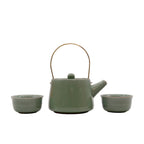Green ceramic teapot with two matching cups on a reflective surface.