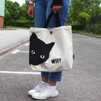 Person holding a tote bag with a black cat design and 'WTF?' text on a street.