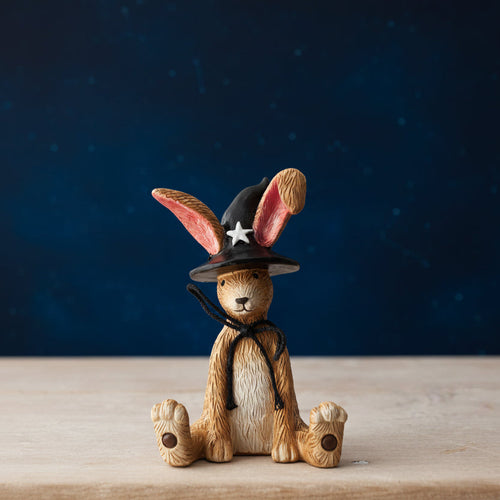 Wooden rabbit figurine wearing a witch hat with a star on a wooden surface