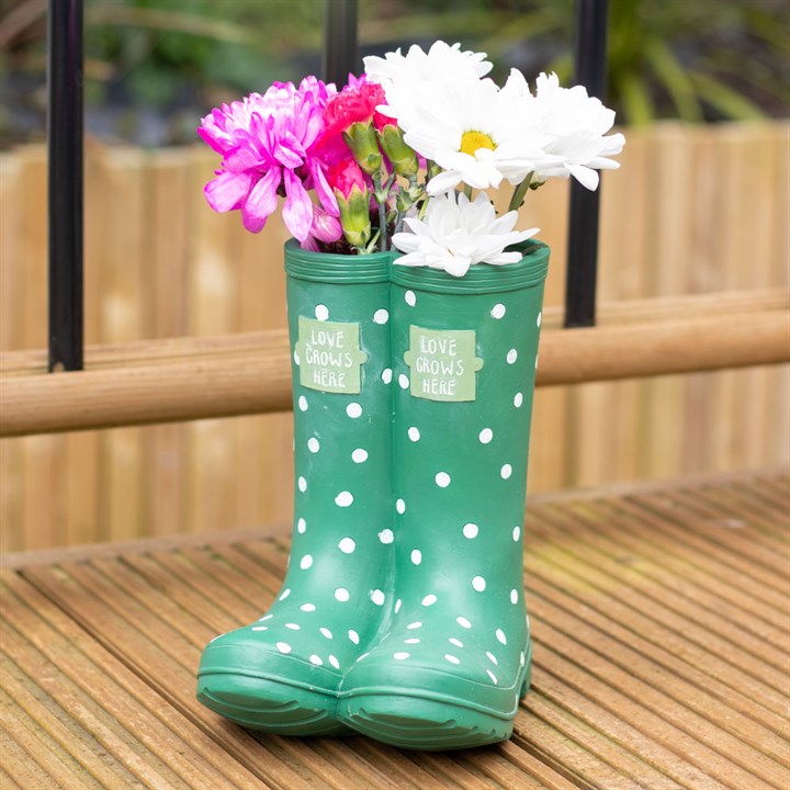 Green polka dot rain boot with flowers on a wooden surface