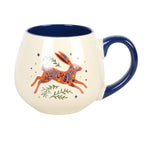 A cream-colored ceramic mug with a dark blue handle, interior, and exterior accents. The front of the mug features a colorful illustration of a jumping hare decorated with floral patterns, surrounded by small green leaves and yellow stars.