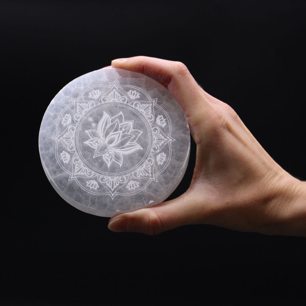 Hand holding a clear selenite plate with a floral design against a black background