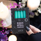 Pack of green candles labeled 'Magic Spell Candles Luck' held by a hand with a blurred candlelit background.