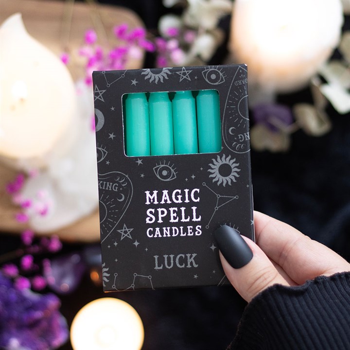 Pack of green candles labeled 'Magic Spell Candles Luck' held by a hand with a blurred candlelit background.