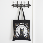 Black tote bag with a cat design and 'Magick Cat Energy' text hanging on a metal hook.