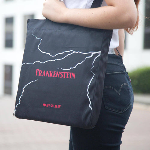 Person holding a tote bag with 'Frankenstein' and 'Mary Shelley' text.