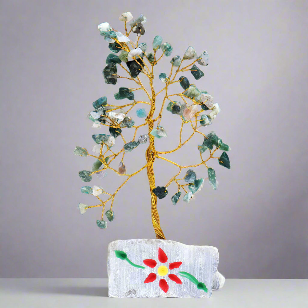 Decorative tree made of stones on a rock with a colourful flower design, against a plain background. Eleanoras