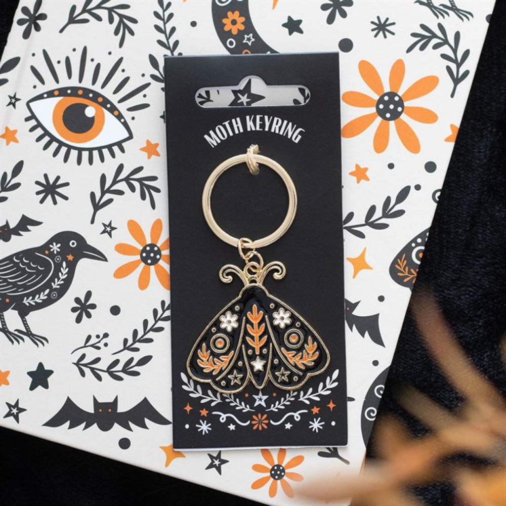 Moth keyring on a decorative card with floral and eye designs.