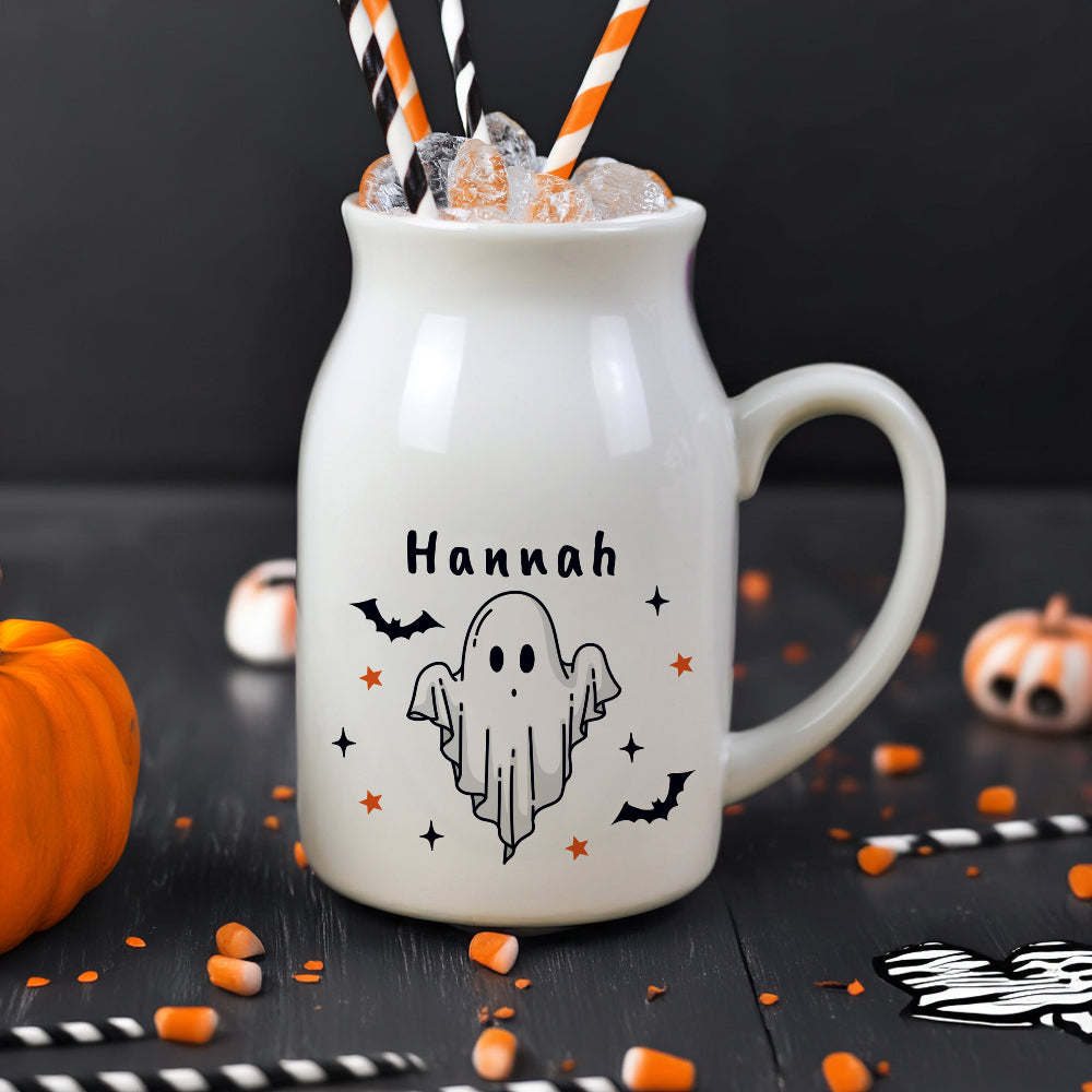 White mug with 'Hannah' and ghost design, filled with Halloween-themed treats on a black background.