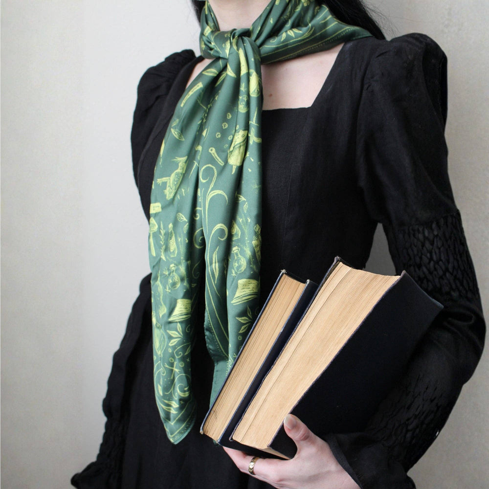 Person wearing a green patterned scarf holding two books against a neutral background