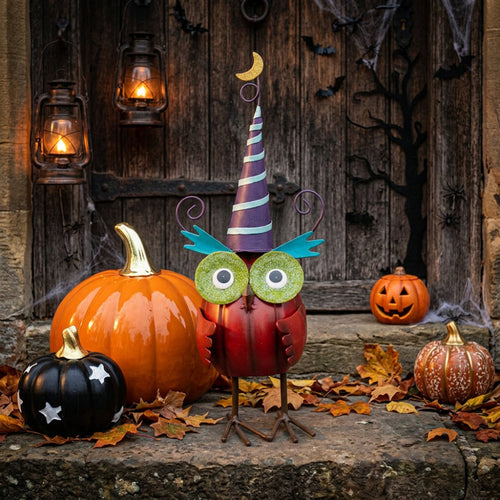 Decorative owl with a colorful hat and googly eyes in front of pumpkins.