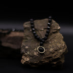 Black beaded necklace with a gold clasp on a dark rock background