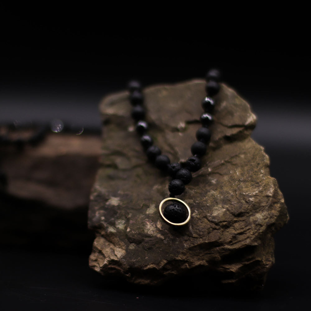 Black beaded necklace with a gold clasp on a dark rock background