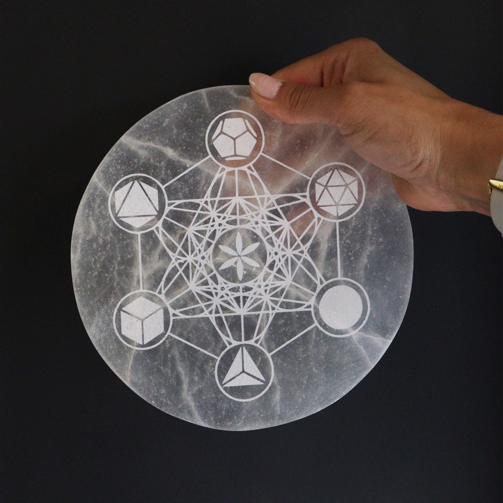 Hand holding a round selenite charging plate with geometric design against a black background