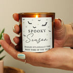 Hand holding a candle with 'Spooky Season' label, blurred background