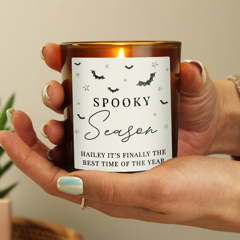 Hand holding a candle with 'Spooky Season' label, blurred background