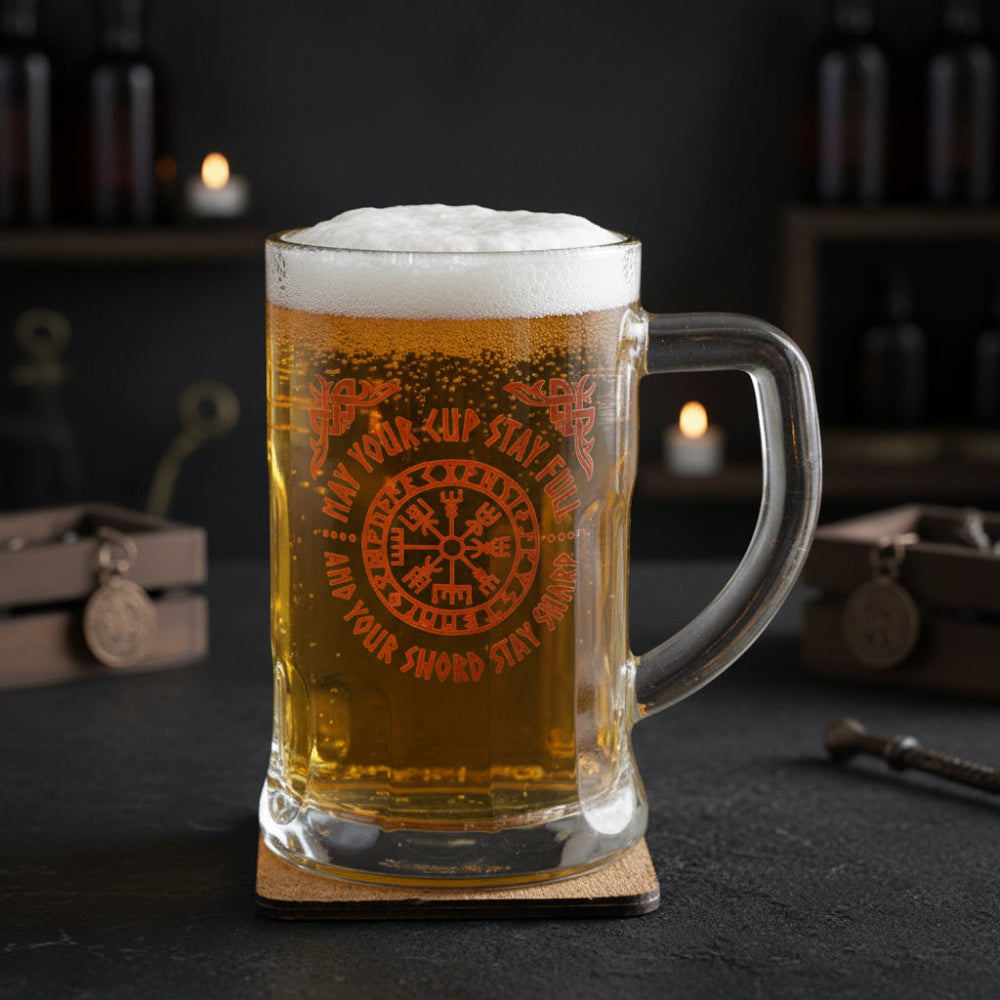 Glass mug with beer and decorative text on a wooden coaster, candle in the background