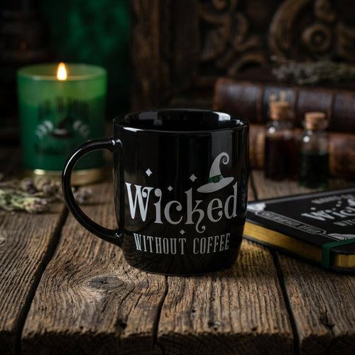 Black mug with 'Wicked Without Coffee' text on a book with a green candle in the background