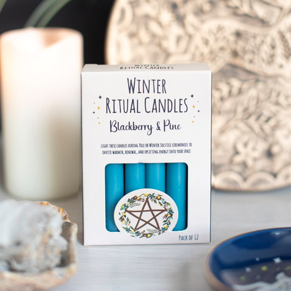 A white box of Winter Ritual Candles, Blackberry & Pine, containing four bright blue candles, styled on a light tabletop with candles and crystals in the background.