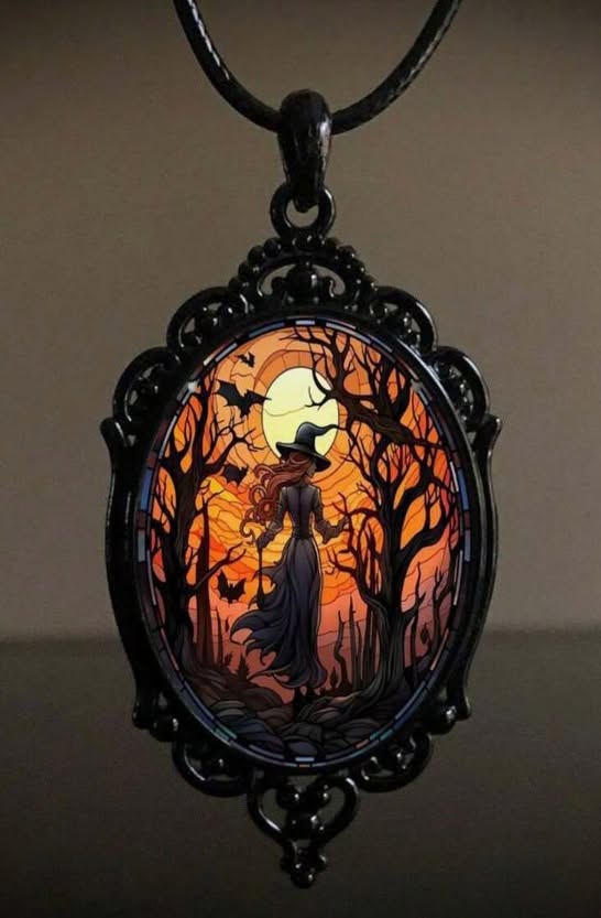A gothic-style oval pendant necklace featuring a witch silhouette in a dark forest at sunset, framed in ornate black metal with a black cord, set against a dark background.