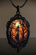 A gothic-style oval pendant necklace featuring a witch silhouette in a dark forest at sunset, framed in ornate black metal with a black cord, set against a dark background.