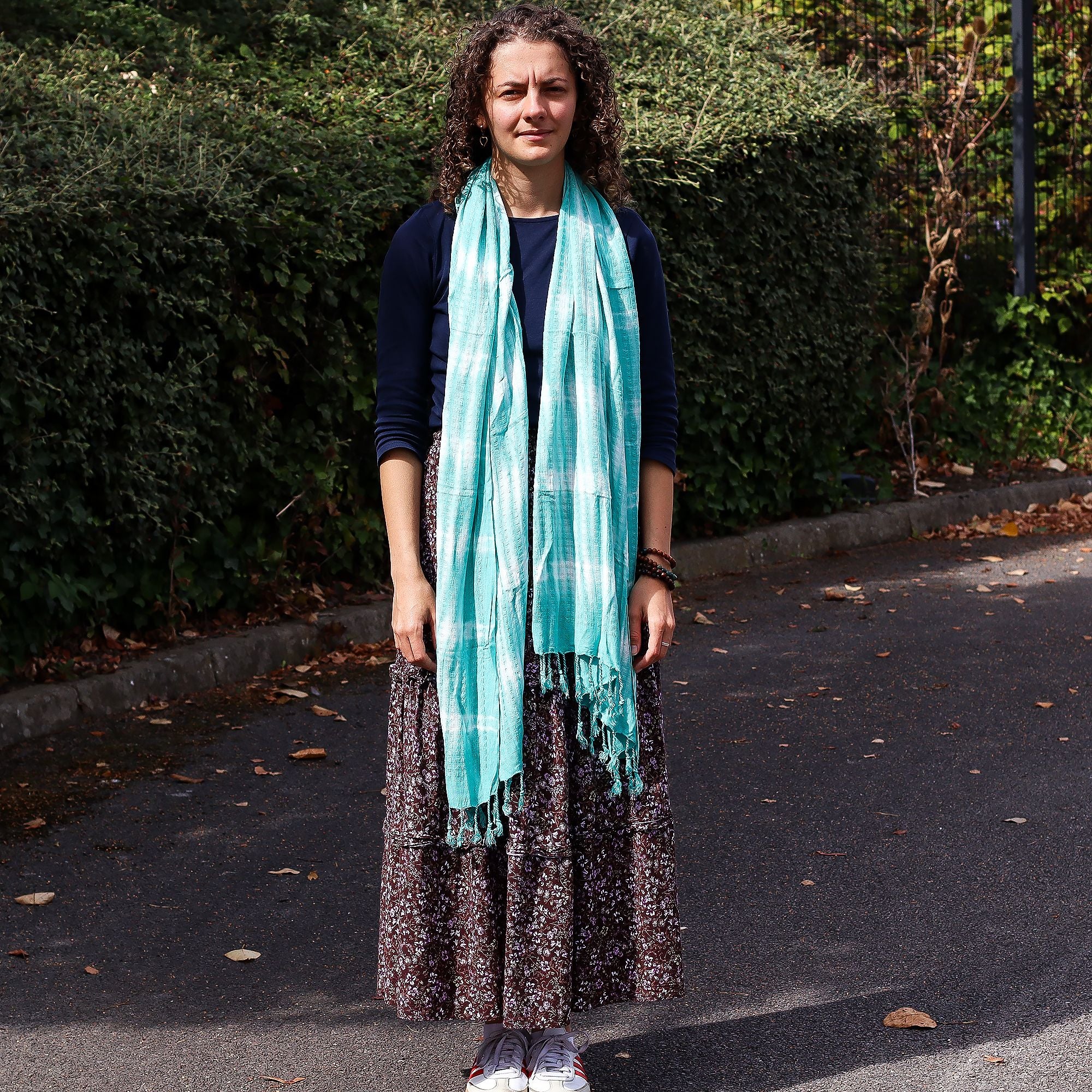 Woman wearing a turquoise scarf standing on a path with greenery in the background