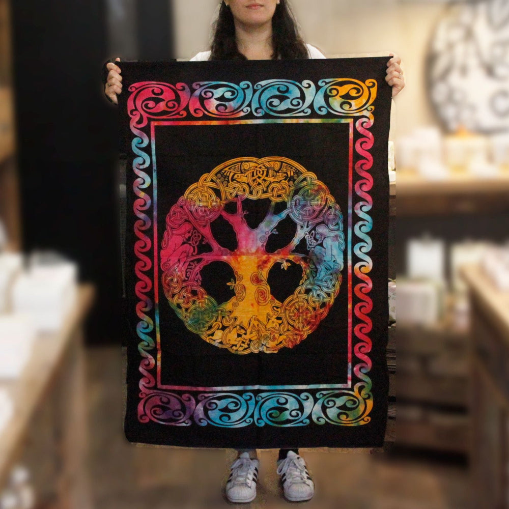 Person holding a colorful tapestry with a peace symbol and tree design.