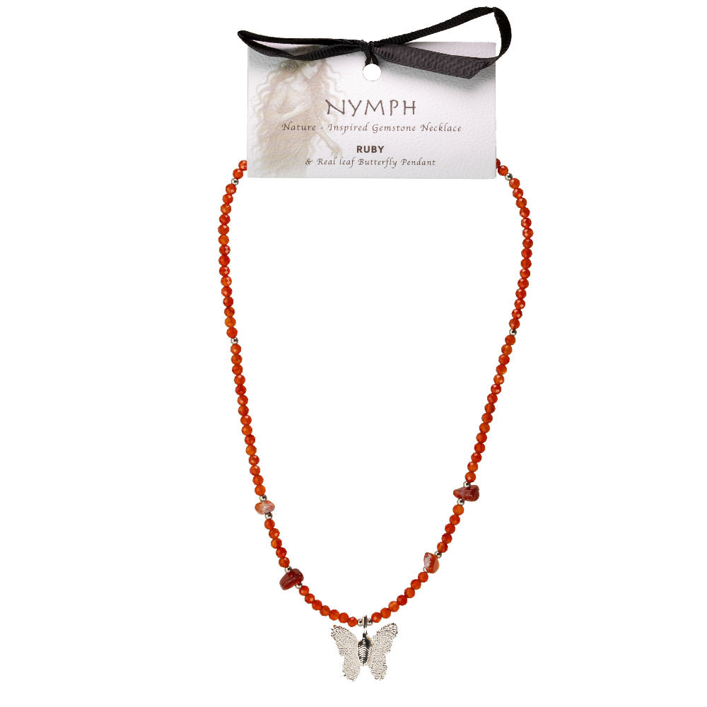 A beaded necklace with red-orange round beads, small polished stone accents, and a silver butterfly pendant, displayed on a branded hang card tied with a black ribbon. The card reads Nymph and Ruby.