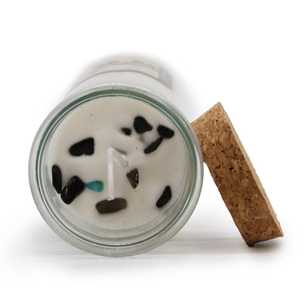 Candle in a glass jar with decorative stones and a cork lid on a white background