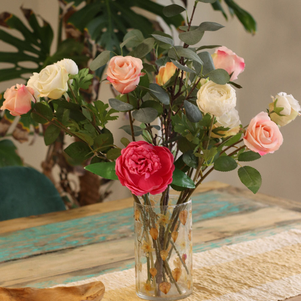 Bouquet of artificial flowers in a clear vase on a textured surface with a blurred background