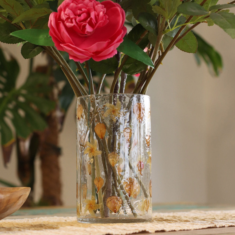Clear vase with floral design containing pink flowers on a wooden surface.