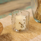 Candle in a glass holder with dried flowers on a woven surface