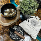 Singing bowl set with 'Flower of Life' design on a wooden surface with a plant and packaging.