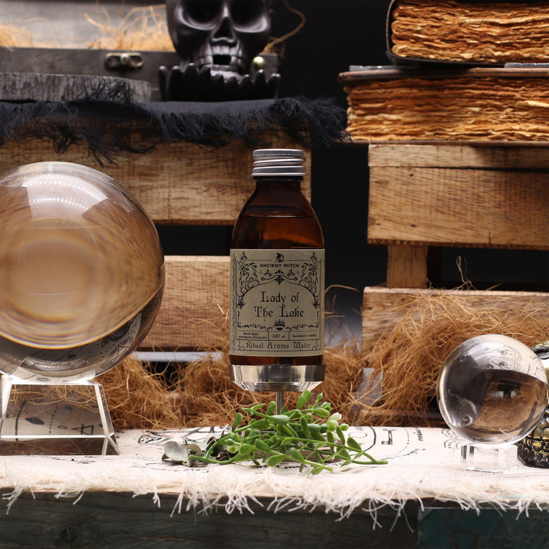 Bottle of 'Lady of the Lake' whiskey with glasses and herbs on a rustic wooden table.