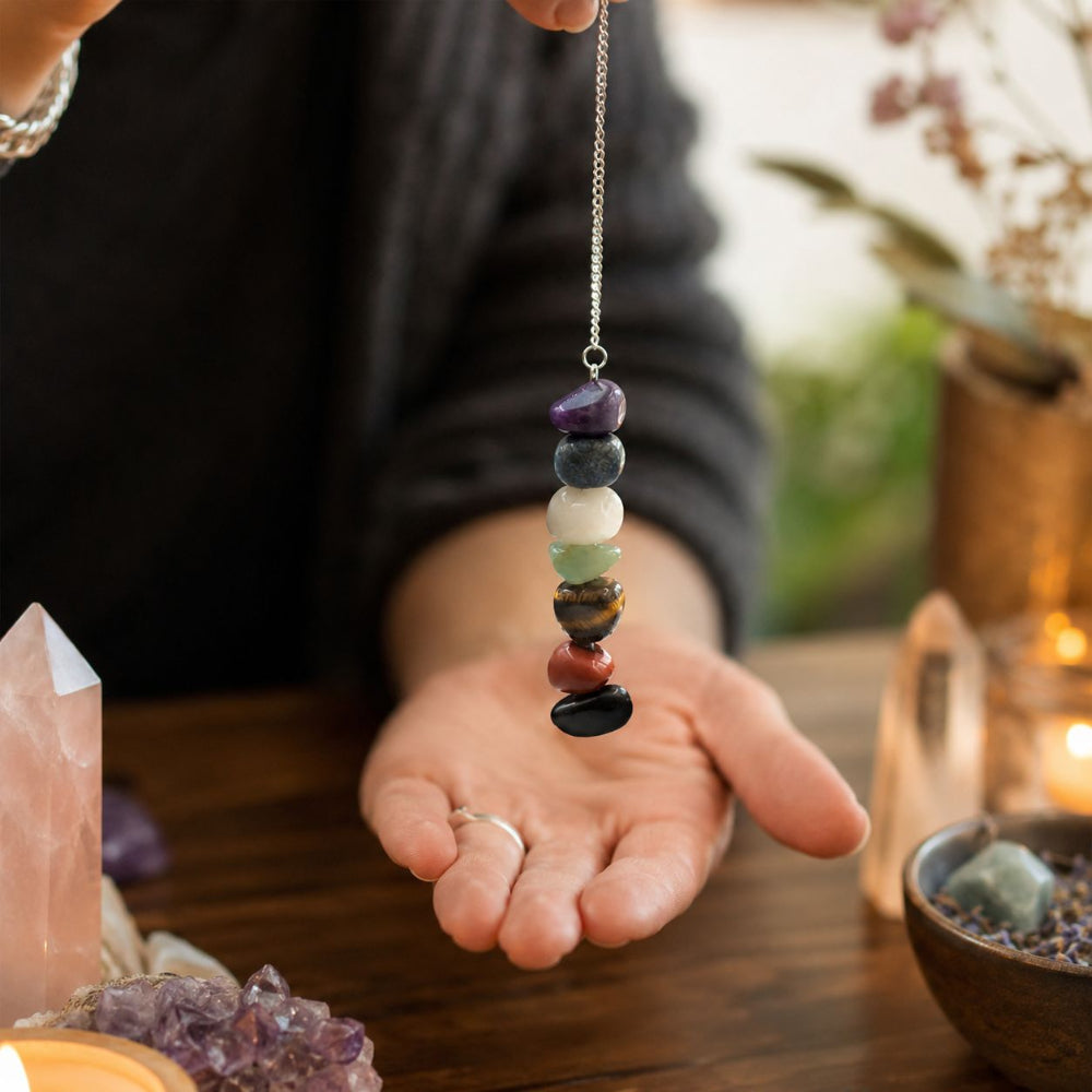 Person holding a pendulum with stones on a wooden surface with crystals and plants.
