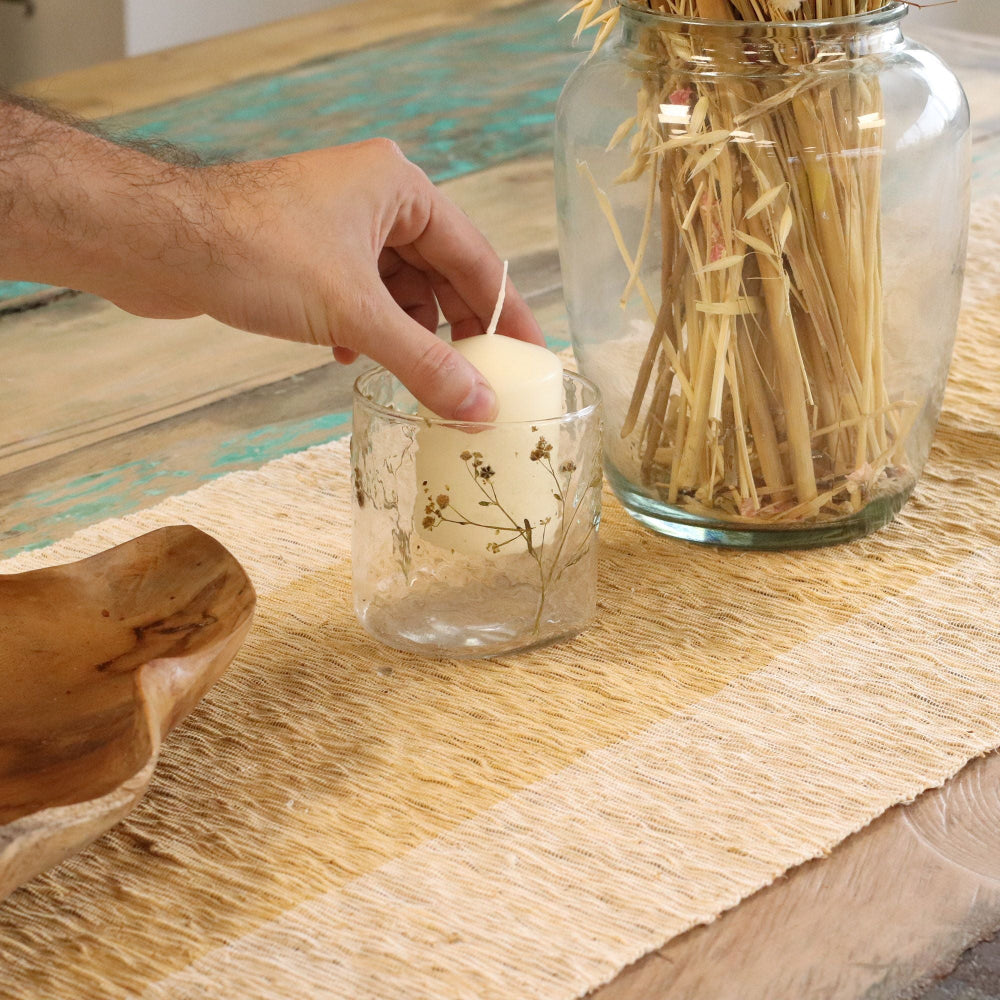 Hand placing a small candle in a glass jar on a wooden table.