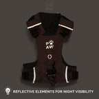 A dark brown dog harness with reflective white stripes and a white paw print logo reading 'PAW AW' on the chest, shown against a dark gray background with text at the bottom stating 'REFLECTIVE ELEMENTS FOR NIGHT VISIBILITY'.